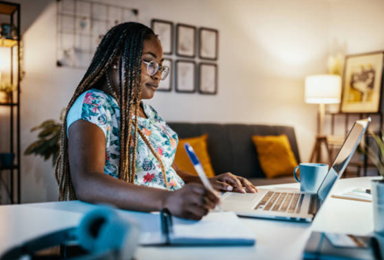 Woman taking notes while reviewing content on a laptop