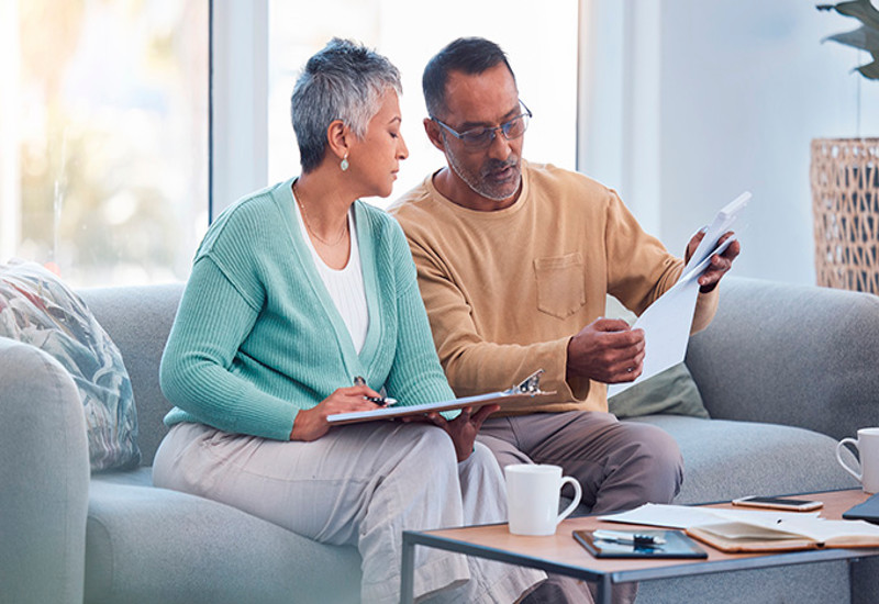 couple at a couch looking at a laptop and financial papers